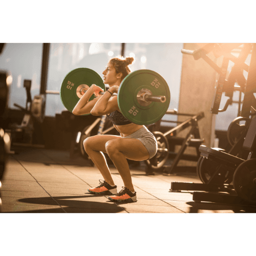 Person performing a front squat with a barbell in a gym, surrounded by exercise equipment.