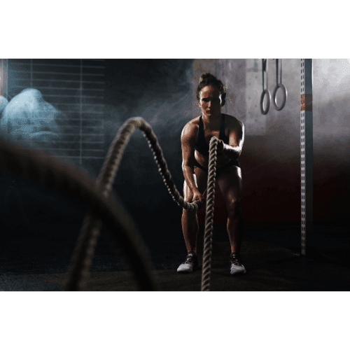 Athletic person performing battle rope exercise in a gym with smoke and workout equipment in the background.