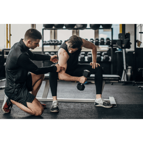 Fitness coach assisting a person performing bicep curls with a dumbbell in a gym.