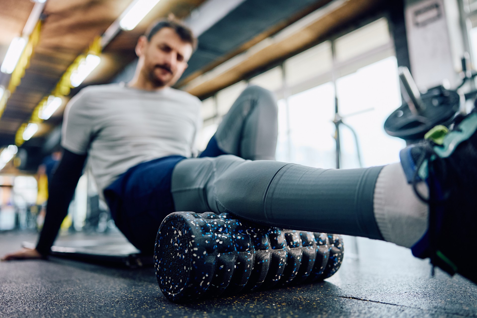 Close up of sportsman doing relaxation exercises with foam roller in fitness center.